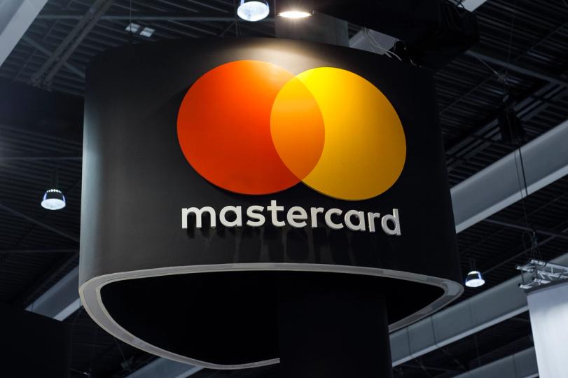 Mastercard logo with a digital currency icon overlaid, against a New York cityscape background.