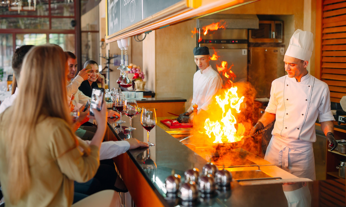 A split image showing a busy restaurant kitchen on one side and abstract AI data streams on the other, symbolizing the intersection of human labor and technology.