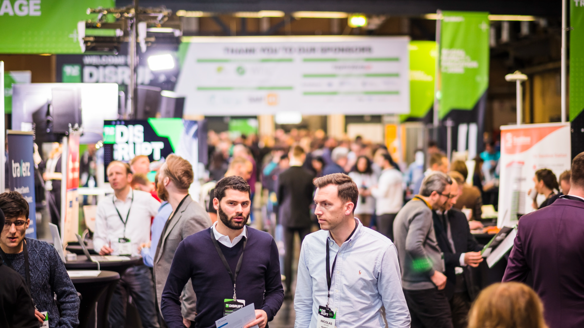 A panoramic view of a bustling expo hall at a tech conference with many startup booths and attendees networking.